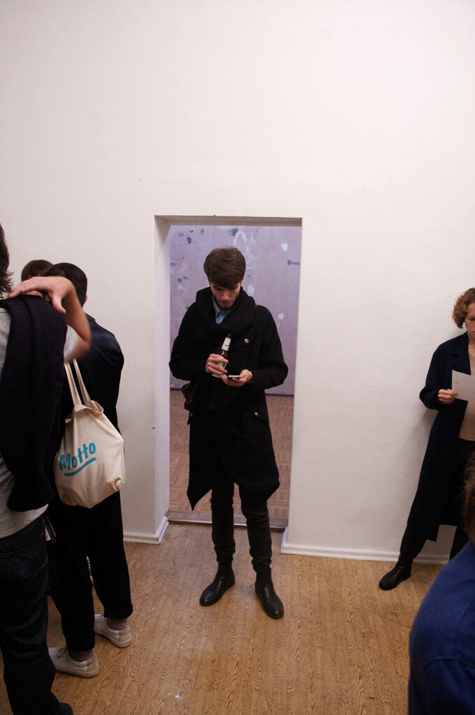local.#non.access opening — a visitor in the doorway of the empty gallery, phone and beer in hand