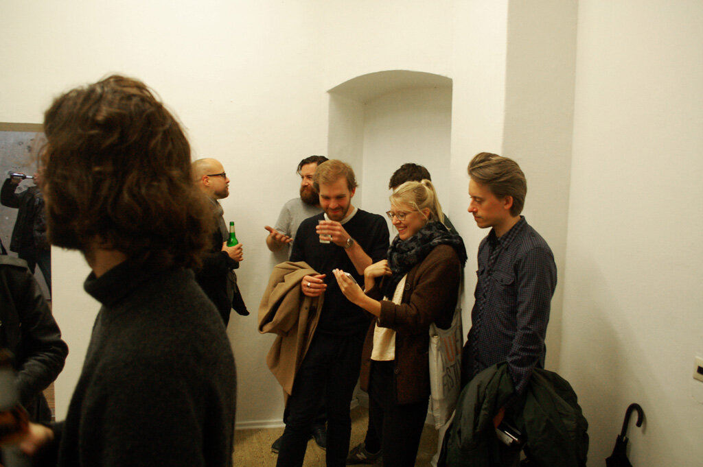 local.#non.access opening — a group in the corner of the gallery, gathered around a phone