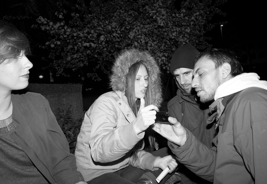 LocalNonOffline — black-and-white: a group sharing one phone at night