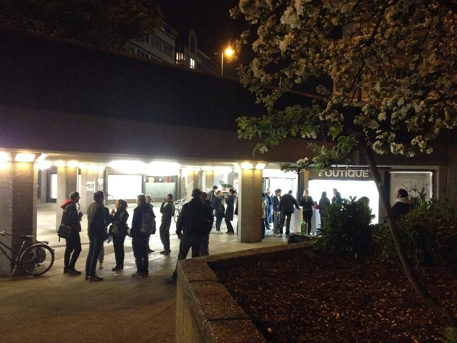 LocalNonOffline — opening night: visitors under the colonnade, a blossoming tree in front