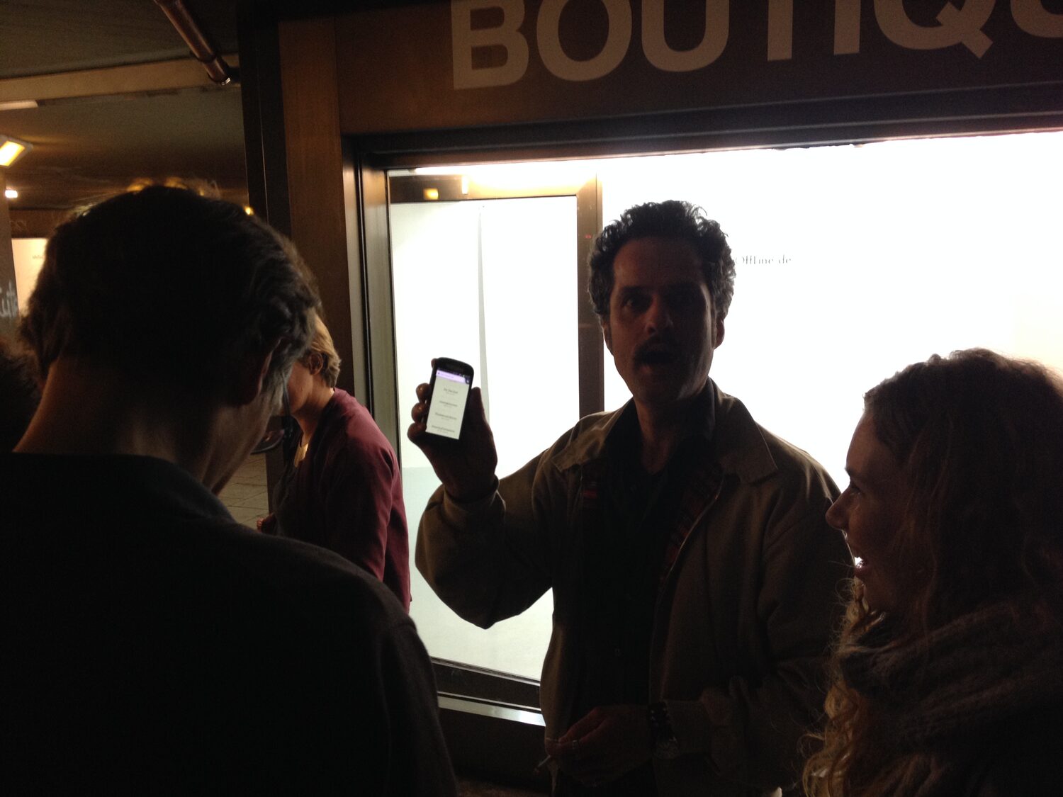 LocalNonOffline — a visitor presents the show on his phone in front of the BOUTIQUE window