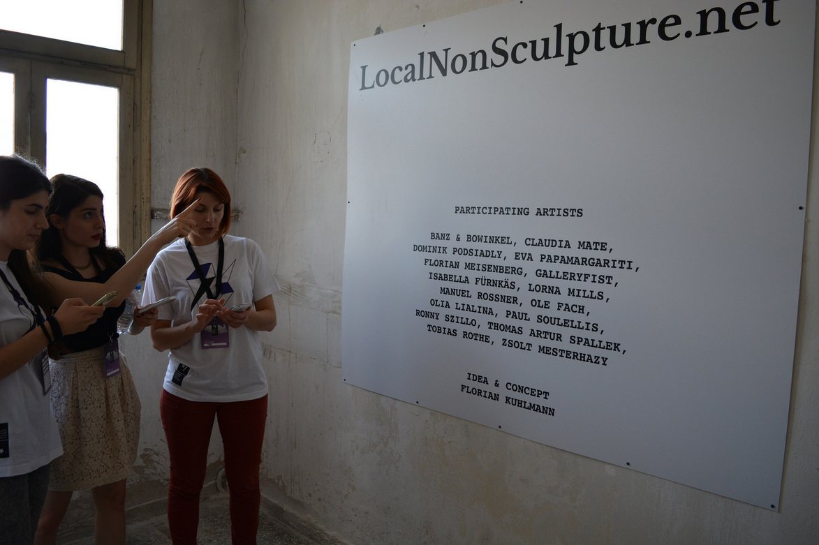 Local #non sculpture — visitors on their phones in front of the 'LocalNonSculpture.net' banner at ADAF